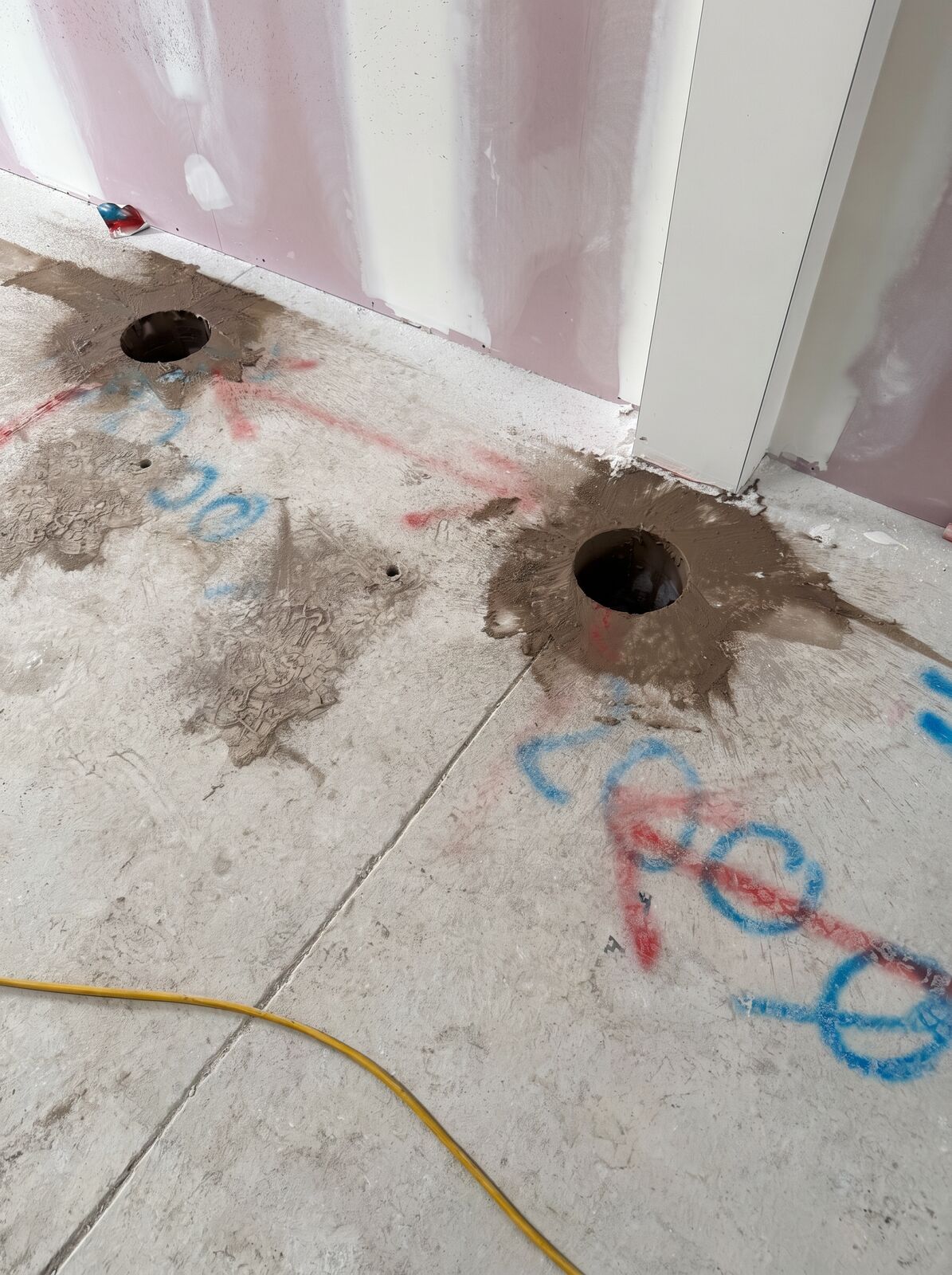 Two clean round cored holes through a concrete floor with setting out marks, on an interior fit out