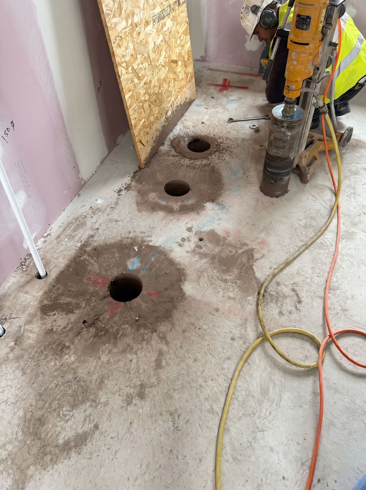 An operator with a hand held core rig and several clean drilled holes through a concrete floor on an interior job