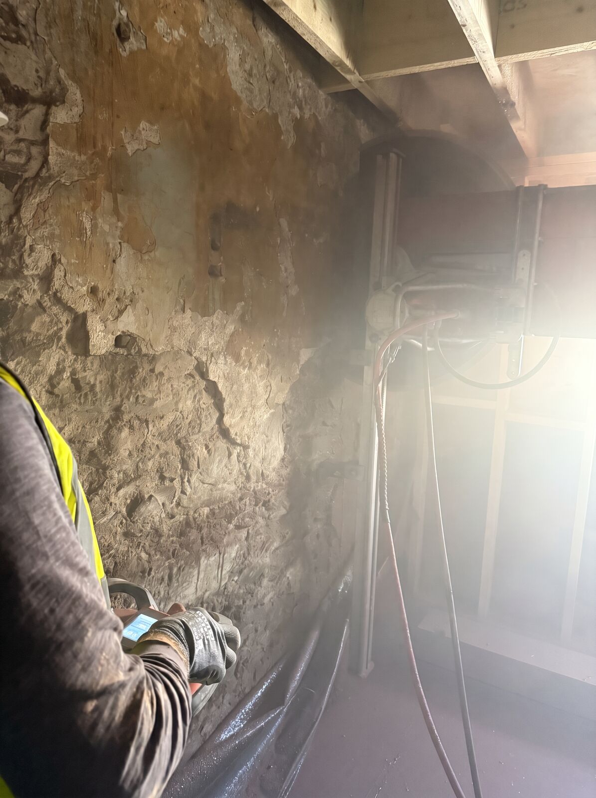 An operative holding the control unit for a wall-saw rig set up against a stripped wall