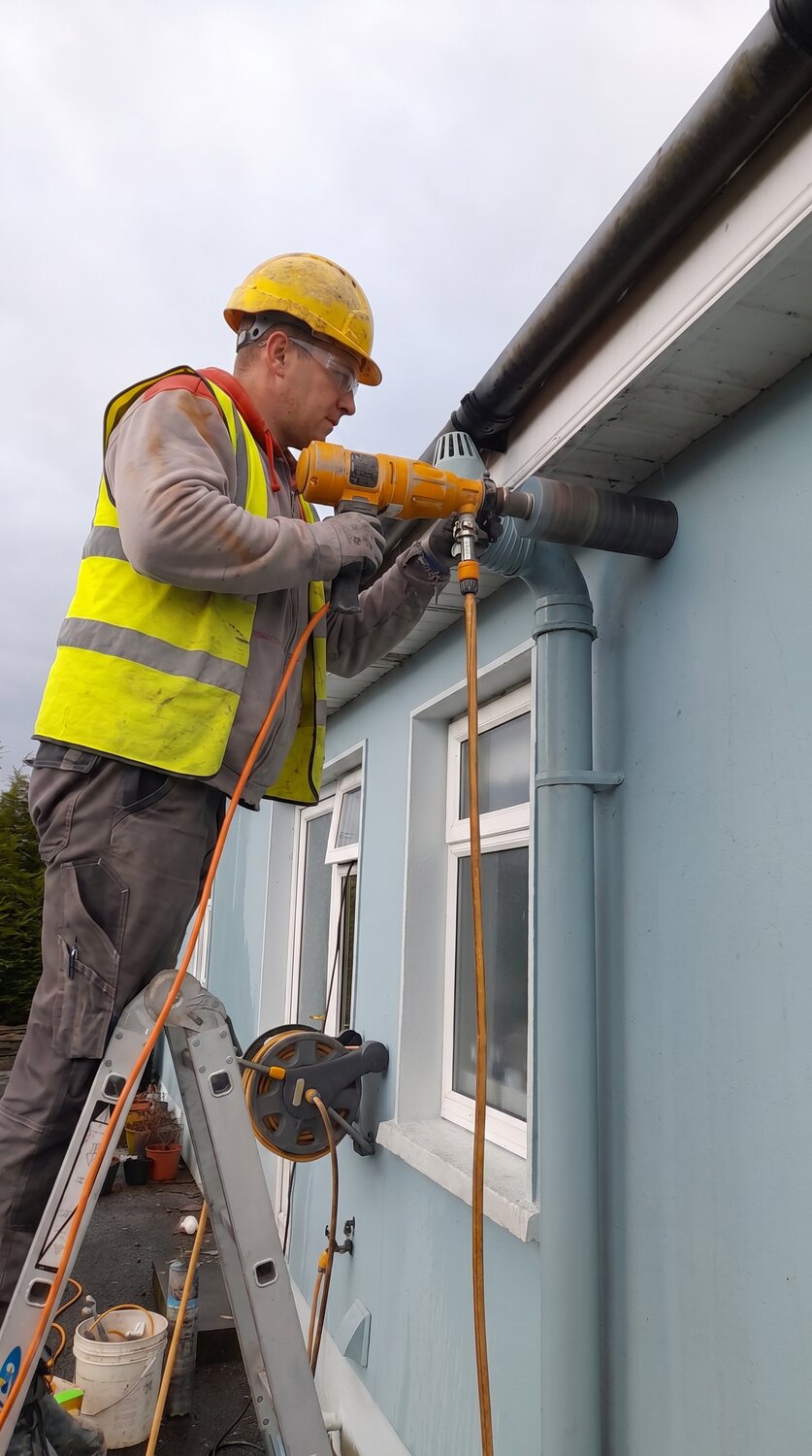 A Munster Core Drilling operator in hi-vis and hard hat core drilling through the eaves of a house from a ladder