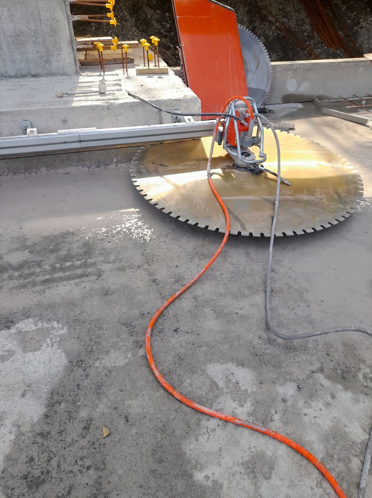 A track-mounted diamond wall saw with a large circular blade set up on a concrete slab on site